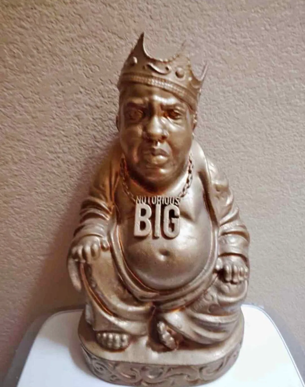 A gold-painted statue of the Notorious B.I.G. seated in the pose of a laughing Buddha, wearing a crown and a “NOTORIOUS BIG” nameplate chain.